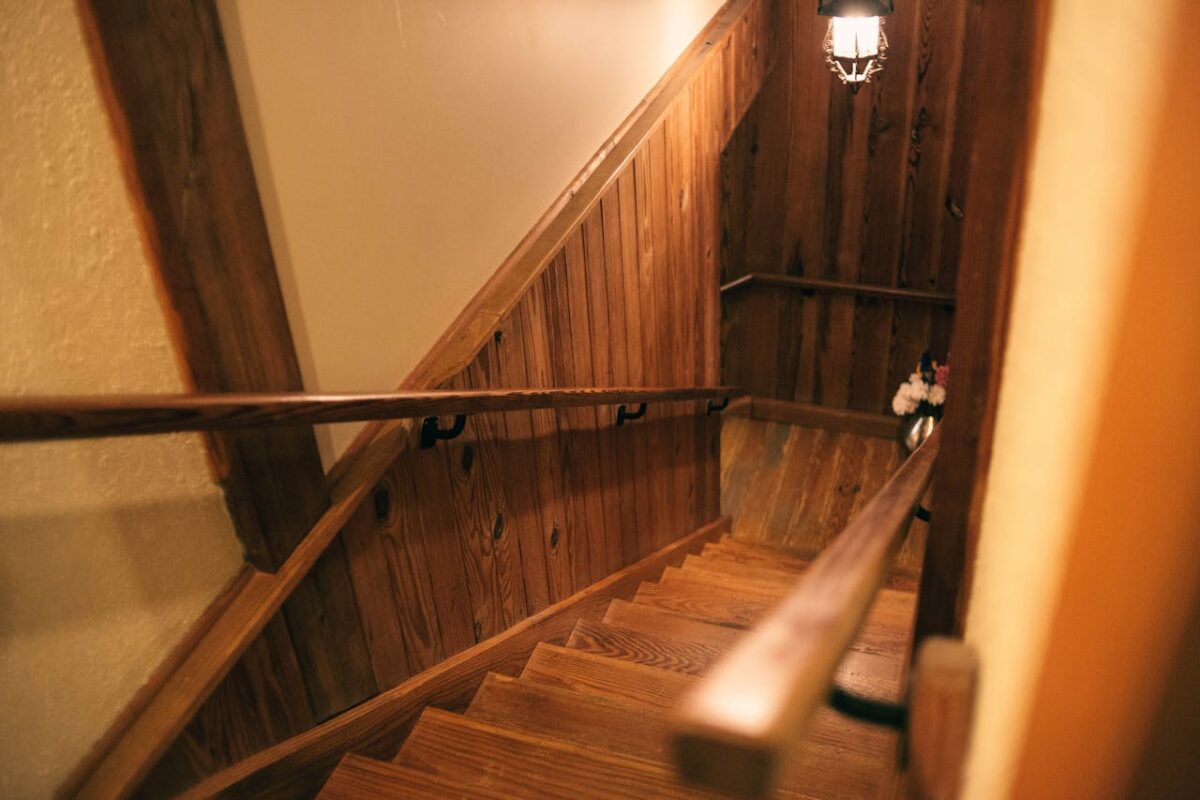 A cozy indoor wooden staircase with handrails under warm lighting, creating a rustic atmosphere.